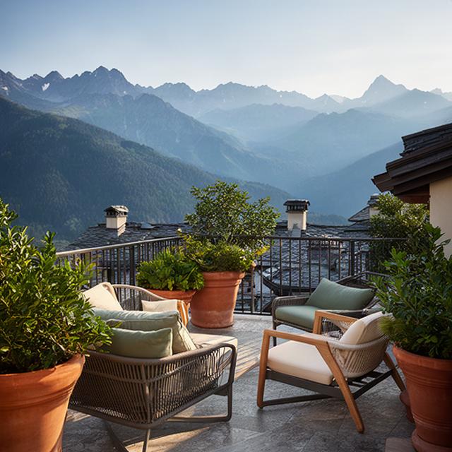 Balcone di montagna arredato con poltrone da esterno, vasi in terracotta e piante verdi